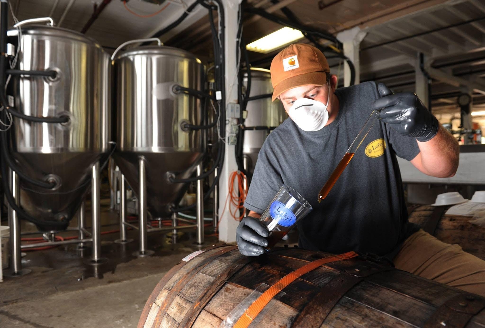 A man with a mask standing over a keg with beer in a long cylinder
